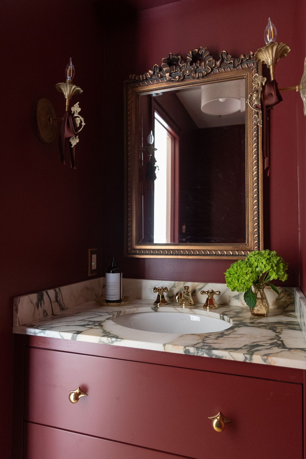 Oxblood powder room with brass sconces and marble vanity